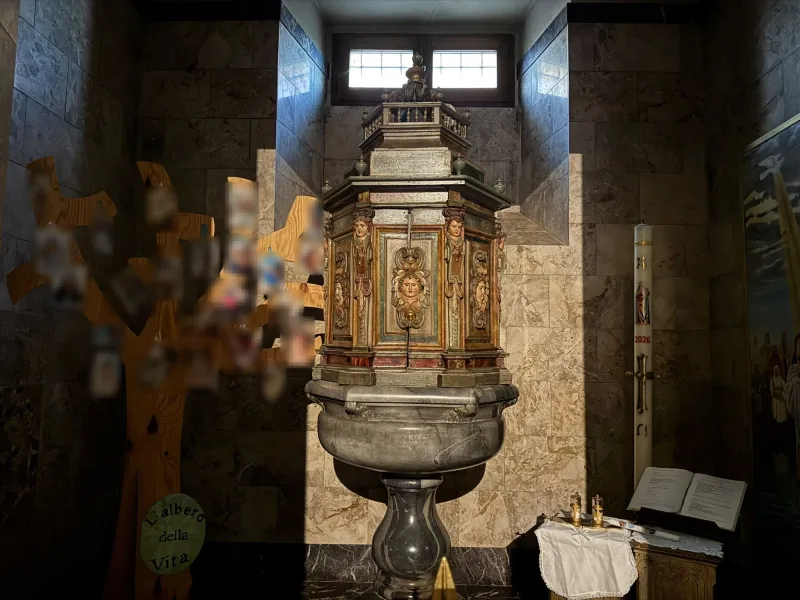 La fonte battesimale: vasca in marmo sotto una copertura in legno intagliato e dipinto. Accanto, l'Albero della vita e il cero pasquale.